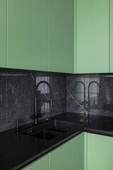 Minimalistic kitchen, black marble wall and table top, green cabinets, black sink with water tap
