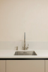 Minimalistic beige kitchen table top and cabinets, stainless steel sink with water tap, against a beige wall