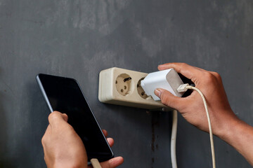 Asian man's hand view plugging a mobile phone charger cable into a wall socket. Ready to connect,...