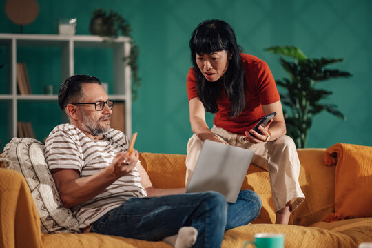 Couple managing budget and bills using laptop and smartphone at home - Powered by Adobe