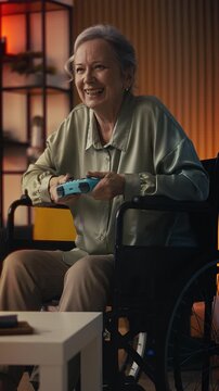 Excited elderly female in wheelchair playing video game with joystick, leisure