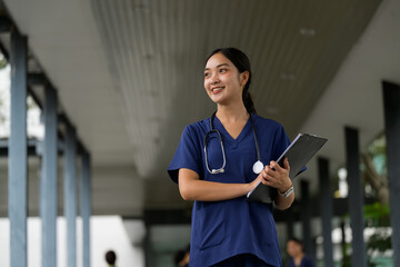 Naklejka na ściany i meble Asian doctor woman smiling, holding clipboard in hospital hallway Naklejka na ściany i meble Asian doctor woman smiling, holding clipboard in hospital hallway
