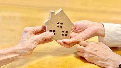 家の小物を女性に渡す高齢女性_黄土色背景