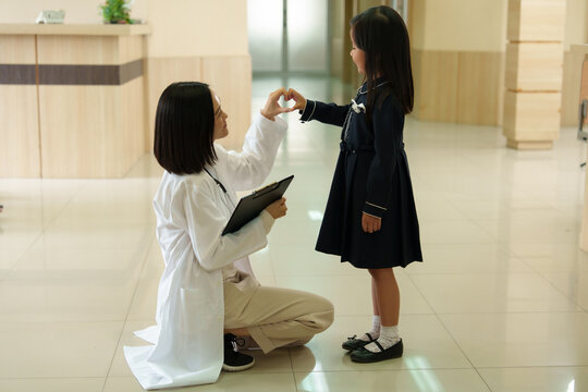 A female doctor is working and standing talking to a young girl in front of the examination room while waiting to examine a patient. - Powered by Adobe