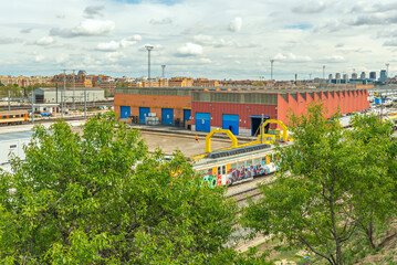Parallel commuter rail tracks crossing a residential area with green acoustic screens integrated into the landscape and elevated pedestrian crossings every 200 meters.
