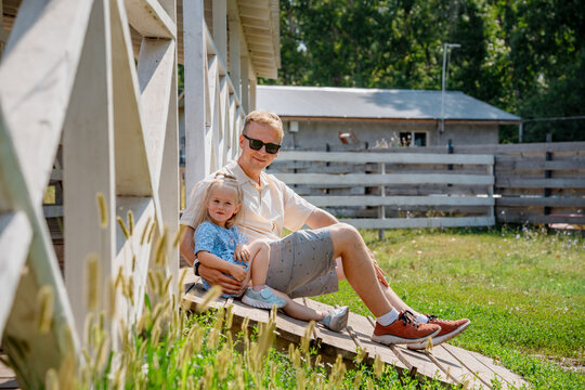 A father sits with his daughter girl child in a beautiful garden on the steps of a house in summer - Powered by Adobe