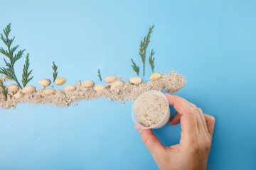 Hand placing sand with container to create seabed with stones and green plant elements on blue background. DIY handmade flat lay composition. Underwater DIY project. Creative flat lay for kids