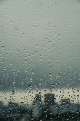 Close-up of raindrops on a window pane with a blurred city skyline in the background on a very cloudy grey da