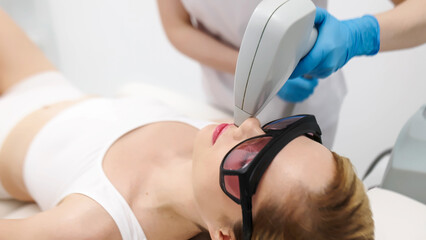 Close-up of a female patient wearing protective glasses during a laser facial hair removal...