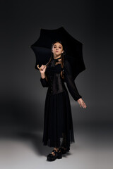 Gothic girl dressed as Wednesday with braids under a dark umbrella for Halloween