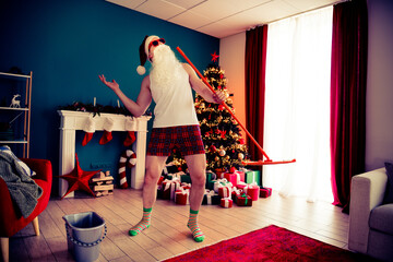 Excited man wearing Santa costume having fun in a cozy Christmas-decorated room with tree, gifts,...