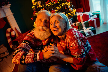 Joyful retired couple shares a warm Christmas moment at home with a decorated tree gifts cozy sweaters and festive lights creating a loving holiday scene