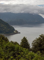 View of the mountains covered in big clouds, sea, and forest