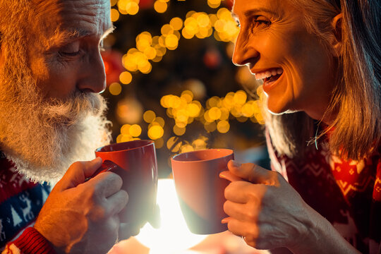 Cozy elderly couple share a warm Christmas moment at home with red mugs smiles and laughter under festive lights creating a dreamy scene of love and togetherness - Powered by Adobe