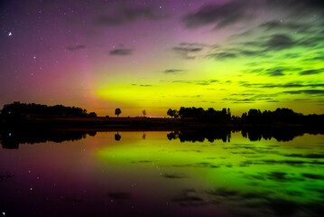 Aurora lights in vivid green and purple glow across the night sky, mirrored perfectly on a calm...