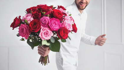 A man in a white shirt holds out a large vibrant bouquet of red and pink roses with a joyful smile.