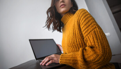 A woman in a warm textured mustard yellow turtleneck sweater looks up from her laptop.