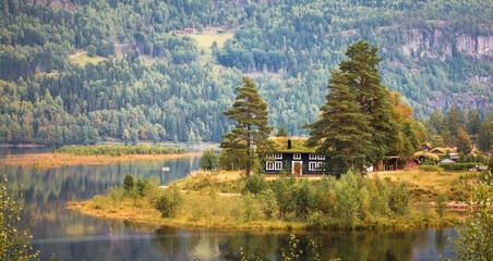 Obraz premium Lakeside harmony in nordic landscape, with traditional house by calm waters, surrounded by green forest and soft autumn colors, a vision of peace and timeless living.