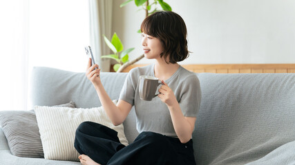 ソファに座ってスマートフォンを使う笑顔の女性