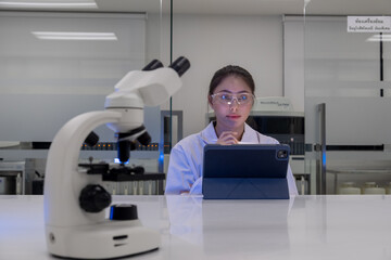 Researcher works in a modern laboratory using a tablet and examining samples with a microscope