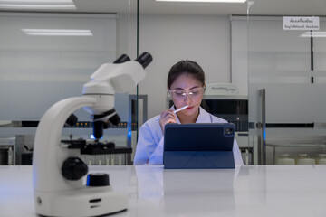 Scientist analyzing data on tablet with microscope in a modern laboratory setting late at night