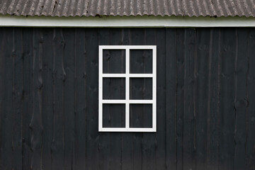 Minimalist white window frame on dark wooden wall exterior.
