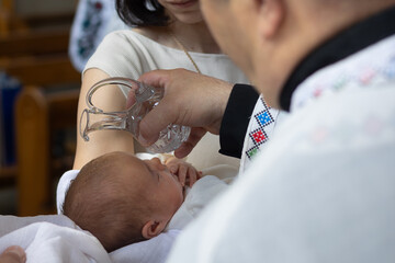 Priest pouring holy water on baby’s head during christening ceremony in Greek Catholic church....