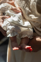 Close-up of newborn baby feet in white christening clothes. Tender moment of baptism, symbol of...