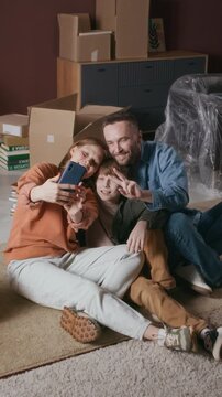 Vertical high angle shot of man showing peace sign while taking pictures with his family after succefully relocating to new apartment
