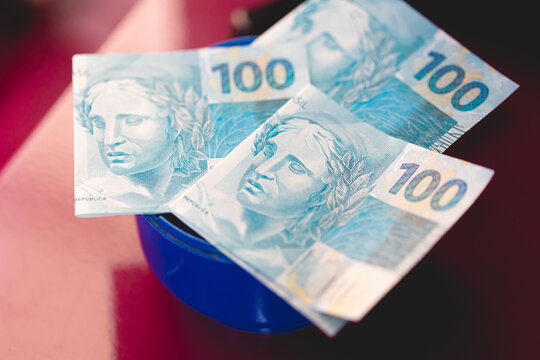 Dinheiro, Brasil, Real. C&eacute;dulas de 100 reais sobre um cofrinho de pl&aacute;stico. Investimento, Selic, Ipca, poupan&ccedil;a, cdb.