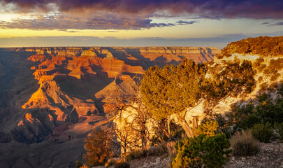 Sunlight casts a warm glow on the rugged cliffs of Grand Canyon as the sun sets, showing deep shadows and vibrant colors in the sky and landscape.
