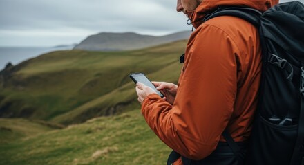 Young caucasian male hiker in orange jacket using smartphone on scenic mountain trail