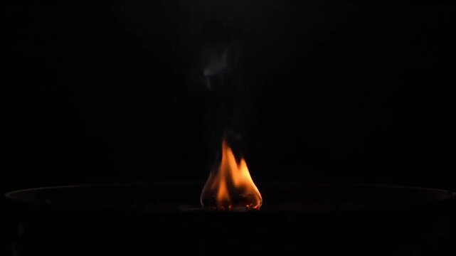 A single flame flickers in the darkness, casting a warm glow.