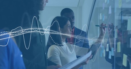 With pulsing waveform on glass wall, business team organizing sticky notes while referencing tablet - Powered by Adobe