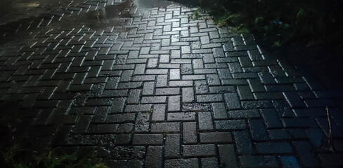 Close-up of wet paving block street at night reflecting light, creating dark moody texture background. Suitable for urban, rainy, or street atmosphere concepts.