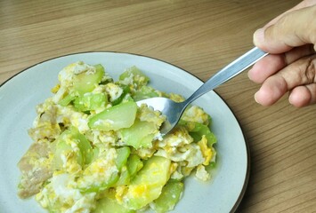 A hand scoops high-fiber angled luffa and egg, a healthy Thai stir-fry that ensures smooth digestion and prevents constipation risks.