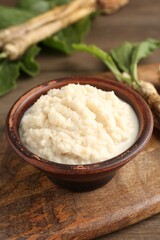 Tasty horseradish sauce and roots on wooden table, closeup