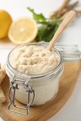 Tasty horseradish sauce, roots and lemons on white wooden table, closeup
