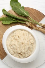 Tasty horseradish sauce and roots on white wooden table, top view
