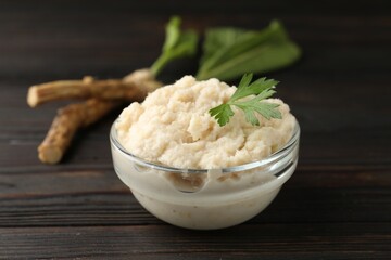 Tasty horseradish sauce with parsley and roots on black wooden table, closeup