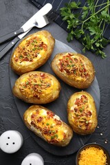Tasty stuffed baked potatoes served on black textured table, flat lay