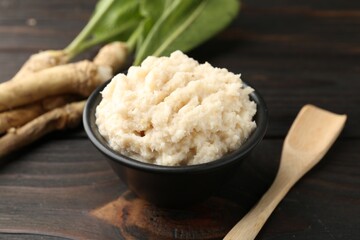 Tasty horseradish sauce and roots on black wooden table, closeup