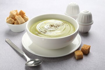 Tasty broccoli cream soup served with croutons on light grey table, closeup