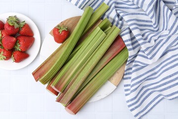 Fresh rhubarb stalks and strawberries on white tiled table, flat lay