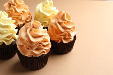 Delicious cupcakes with colorful cream on beige background, closeup. Space for text