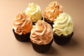 Delicious cupcakes with colorful cream on beige background, closeup