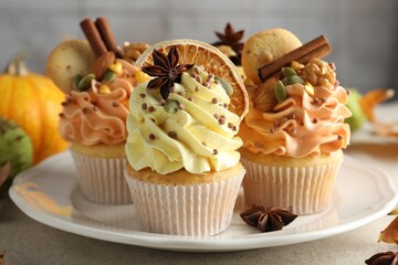 Delicious cupcakes with colorful cream, spices, cookies, nuts and autumn decor on grey table, closeup