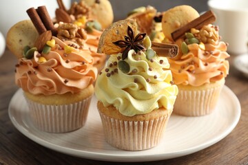 Delicious cupcakes with colorful cream, spices, cookies and nuts on wooden table, closeup