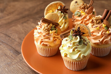 Delicious cupcakes with colorful cream, spices, cookies and nuts on wooden table, closeup. Space for text