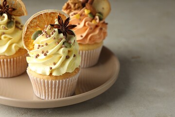 Delicious cupcakes with colorful cream, spices and nuts on grey table, closeup. Space for text